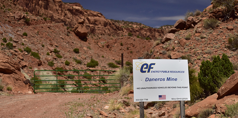 Daneros mine sign in front of closed gate between rocky hills