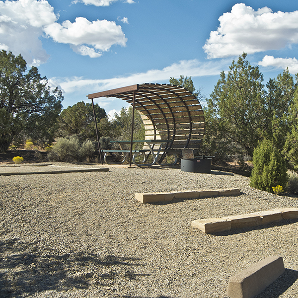 A curved shade structure and picnic table at an empty site at Hovenweep Campground