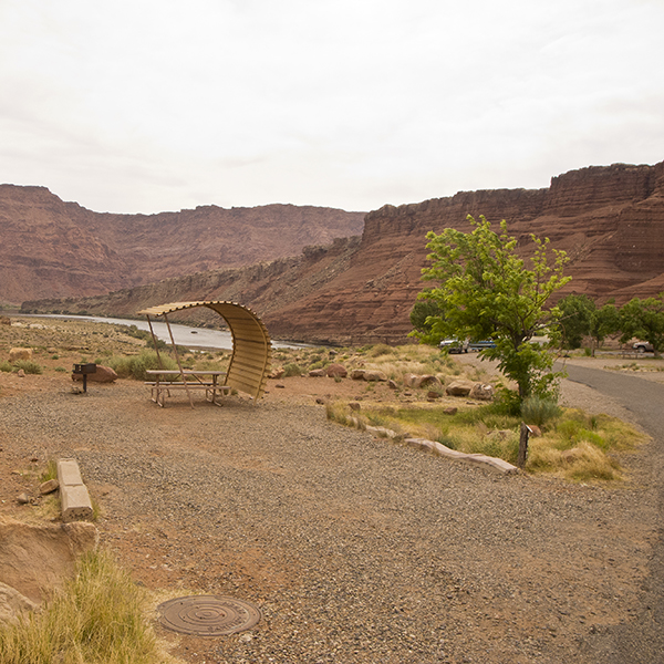 An empty campsite at Lees Ferry Campground with a picnic table and shade structure and views of the Colorado River.