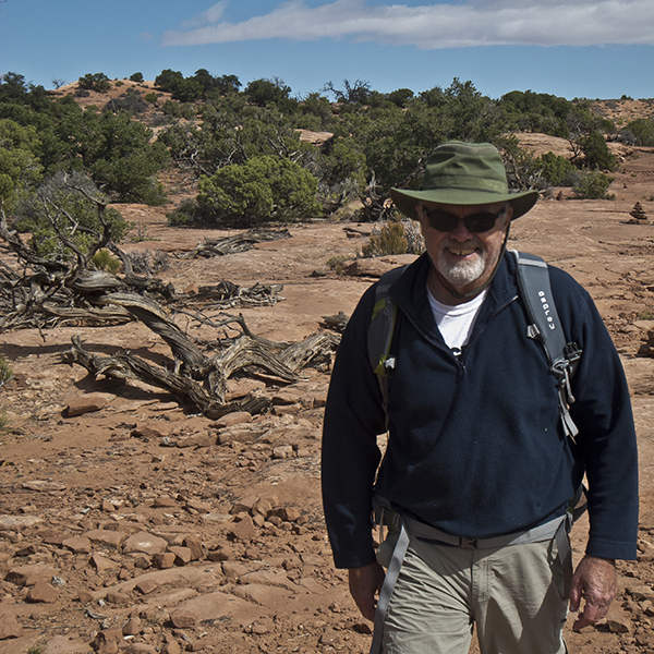 A man in a green hiking hat walks across red slickrock