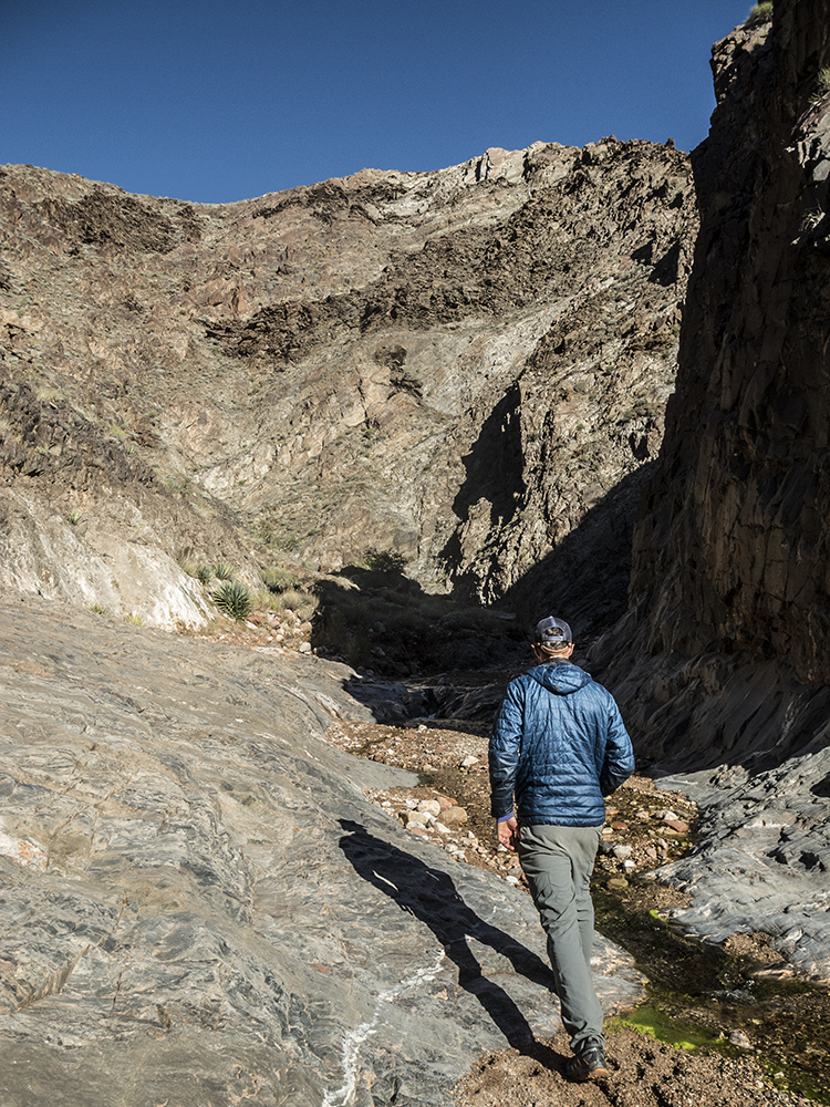 A view of the lower section of Boucher Creek, with a male hiker wearing a blue jacket walking up the creek.