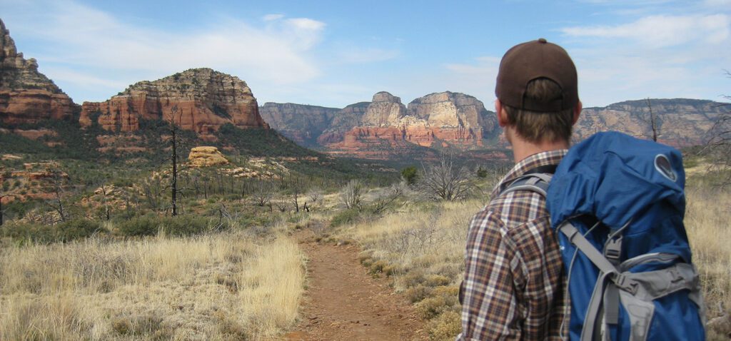 A male hiker with a blue back looks down the trail toward cliffs