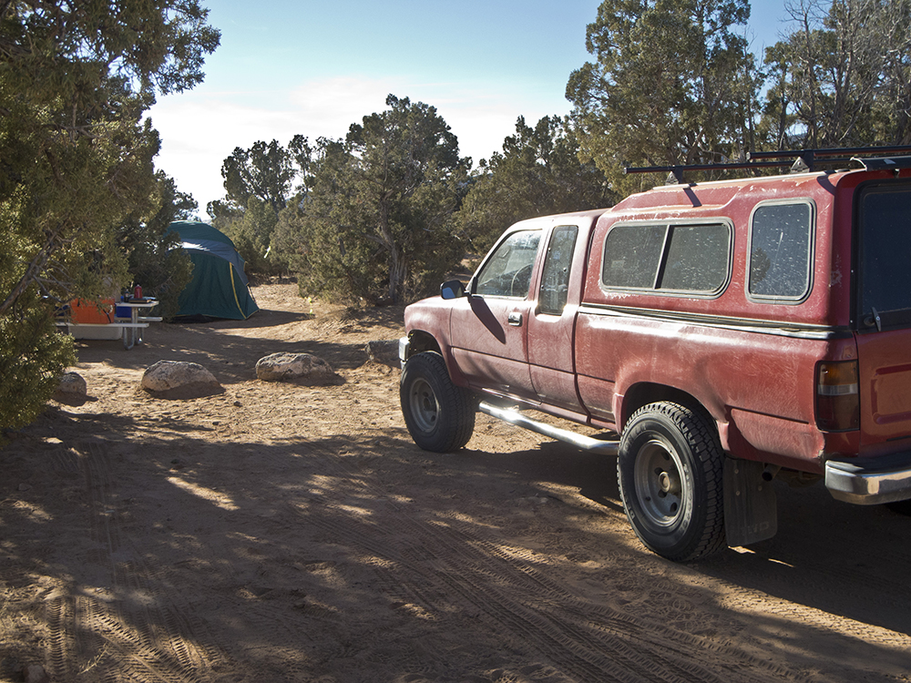 A red truck with a camper shell parked in a campsite at Cedar Mesa Campground