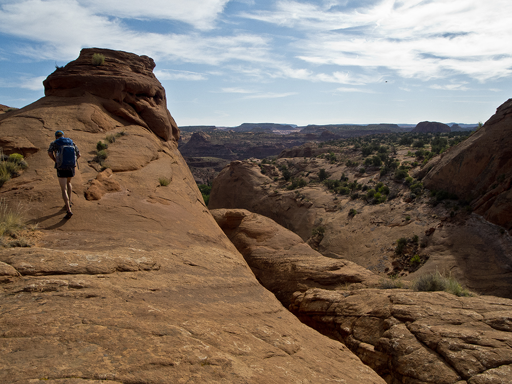 A hiker climbs a sandstone dome.