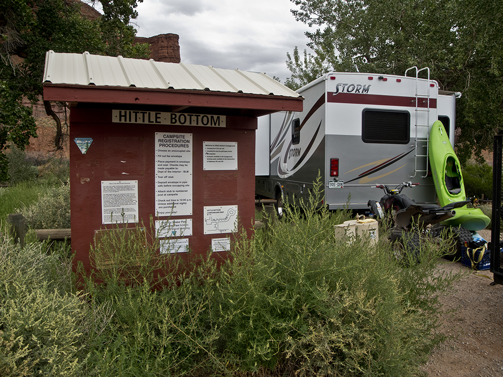 An RV with a green kayak resting up against it next to an information board for Hittle Bottom Campground