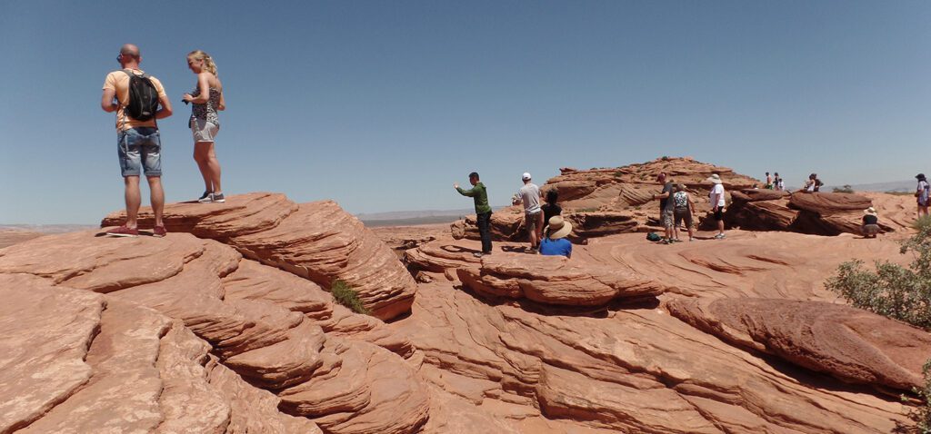 Tourists standing on sandstone slabs at the canyon rim.