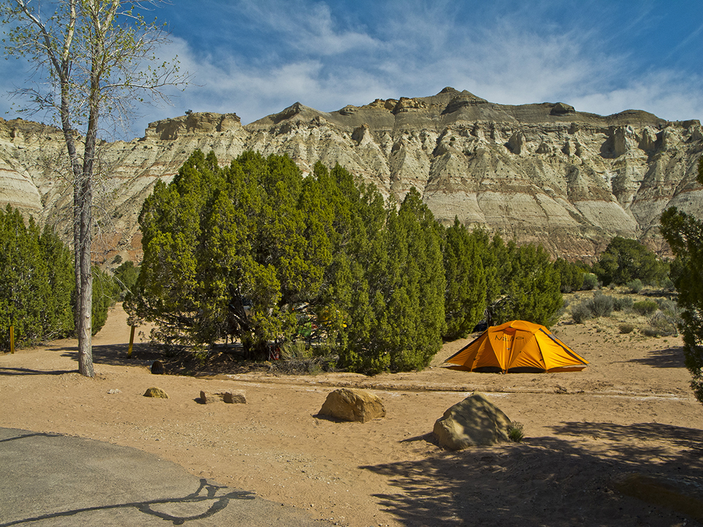 An orange tent, green bushes, and grey cliffs in the background