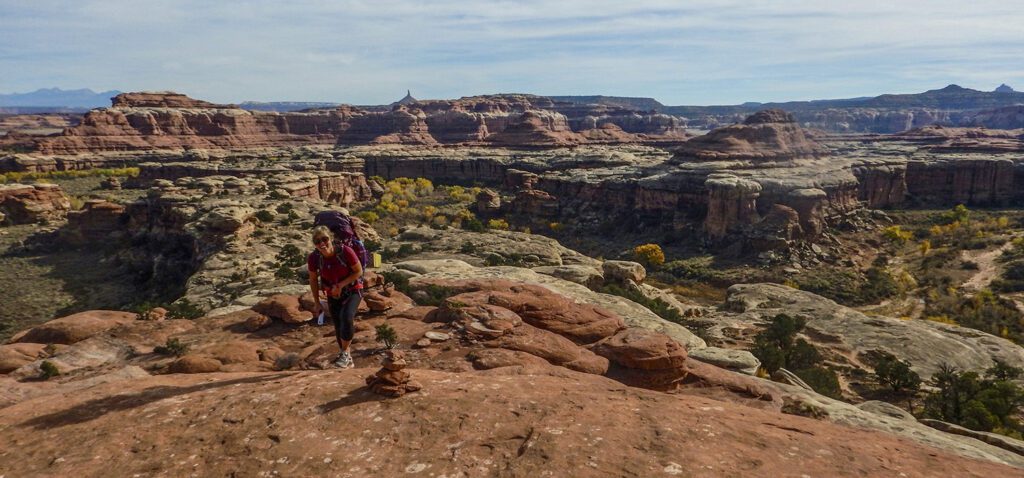 A woman hiker in a pink shirts walks across orange slickrock