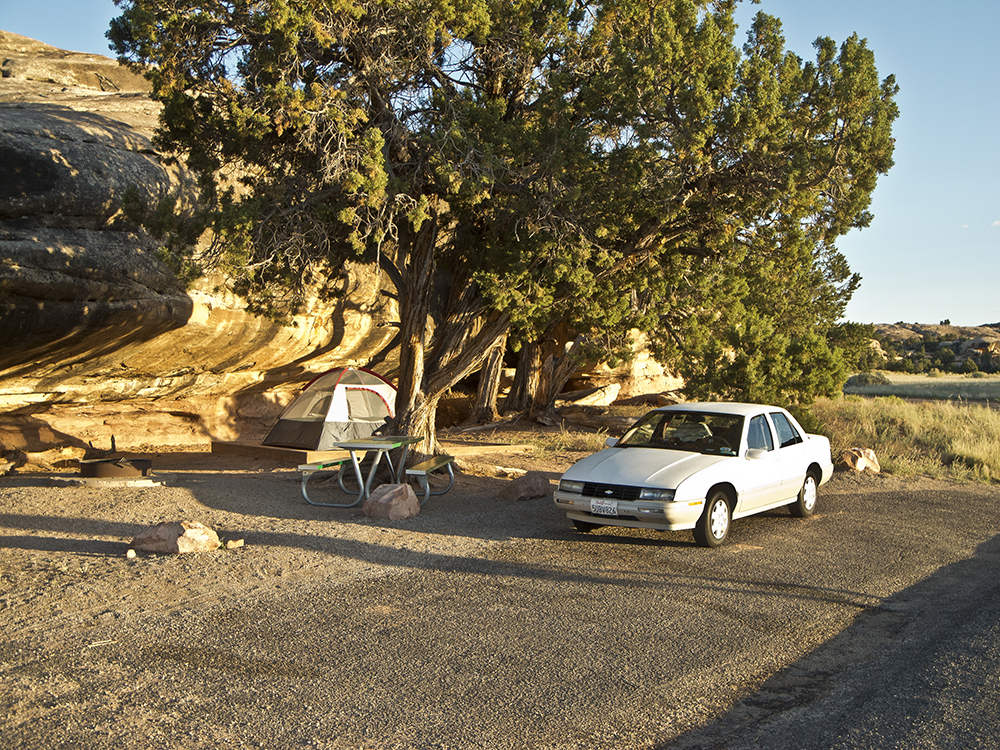 A white sedan parked next to a campsite