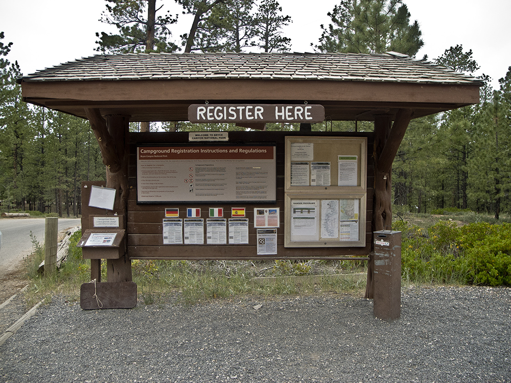 Brown campground entrance board, with "register here" in bold letters