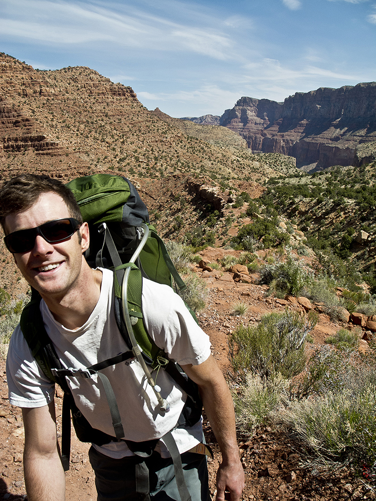 A male hiker wearing sunglasses smiles as he heads up the Tanner Trail