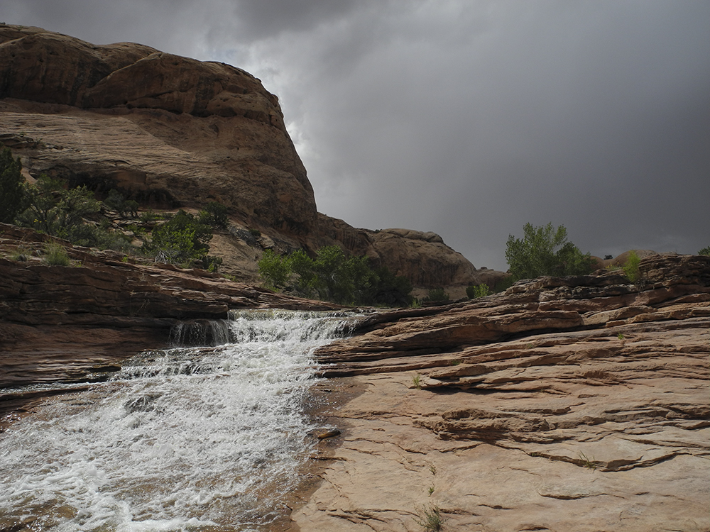 A creek cascades over the slickrock floor of a canyon