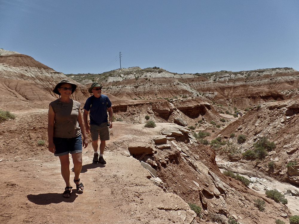 A man and woman walk on a red sandstone bench