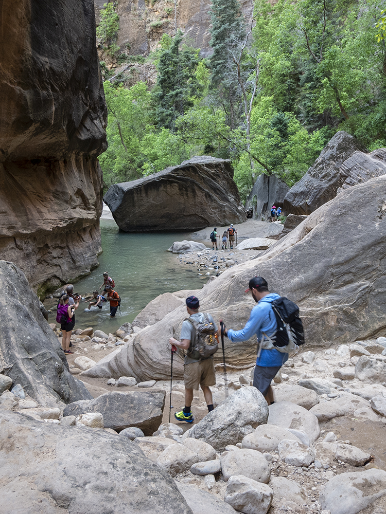 Hikers descend a rocky trail to a pool in the Narrows