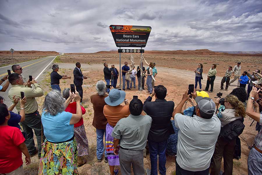 Tribal leaders stand below bears ears national monument sign at the unveiling while a crowd looks on and takes pictures