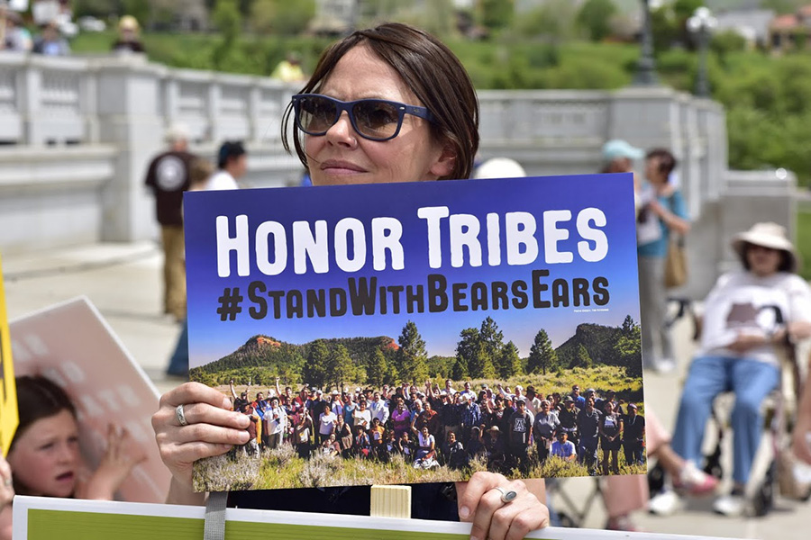 Woman in sunglasses holds a sign that says Honor Tribes