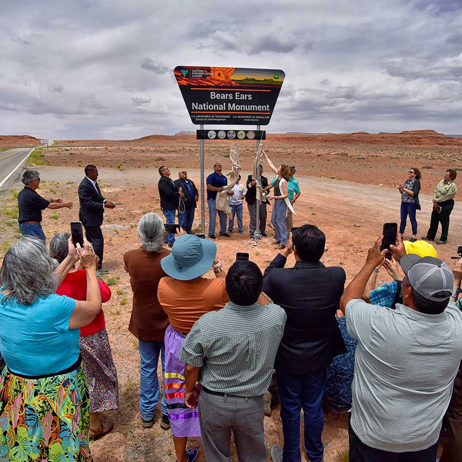 A group of tribal leaders unveil a new Bears Ears National Monument sign while a group of supporters cheer and look on.