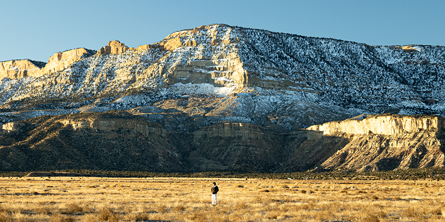 Snow covered mesa with small figure standing in an empty field below