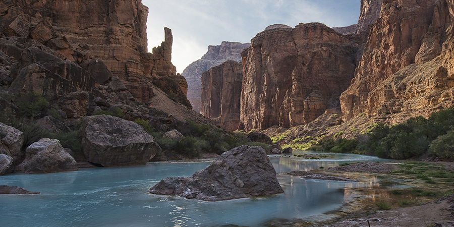 Brilliant carbonate blue water at the Salt Trail campground along the Little Colorado River with reddish cliffs rising