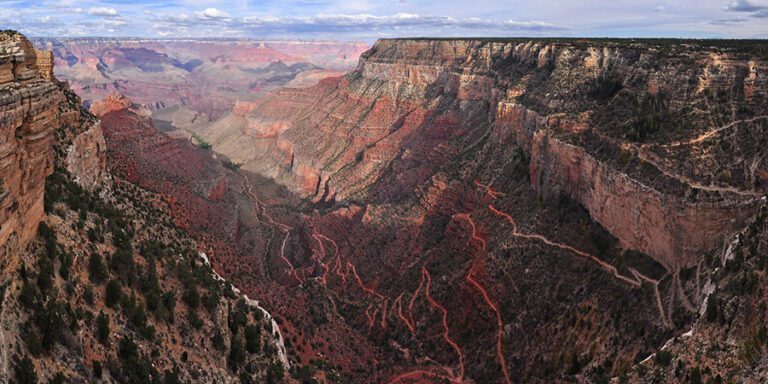 Steep switchbacks carve down the cliffs of the Grand Canyon in zigzag patter, red dirt trails