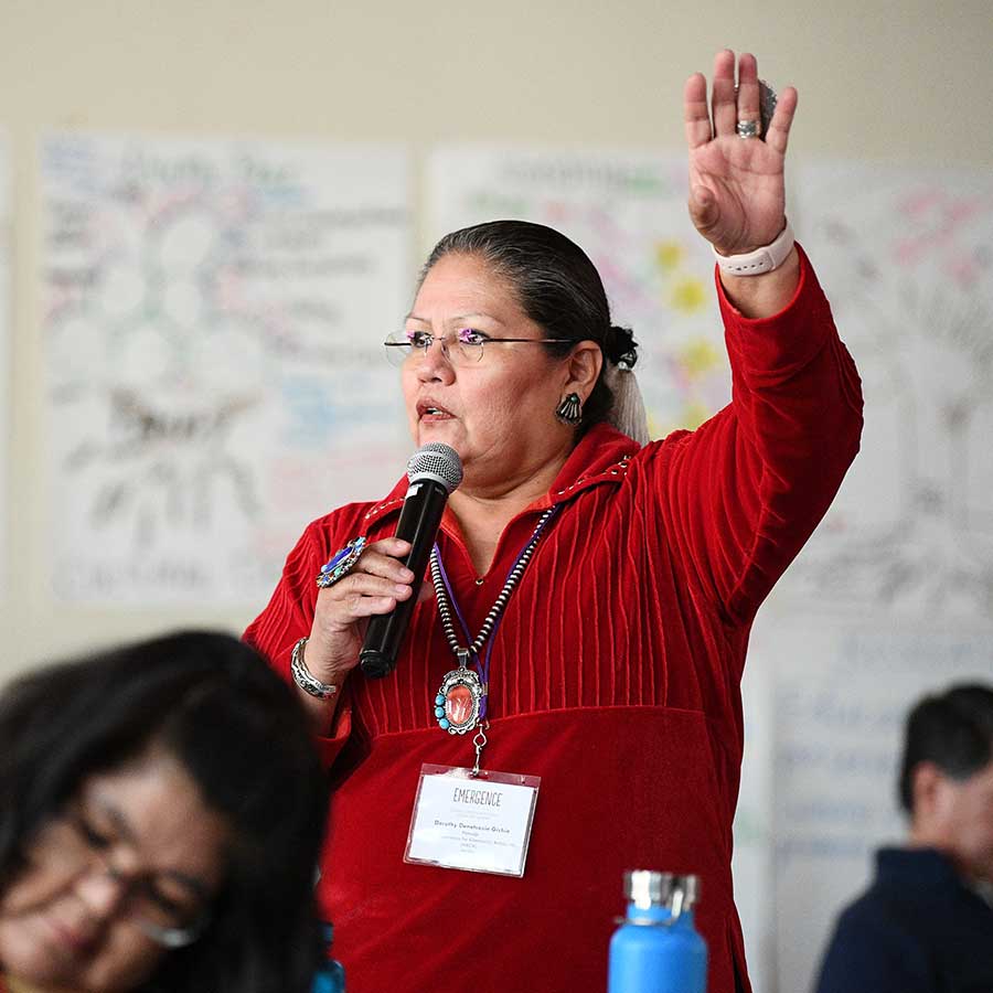 A woman in red speaks into a microphone while gesturing with one hand in the air