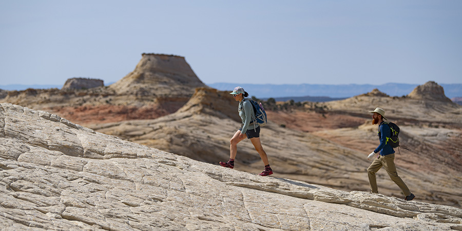 A man and a woman hike up a stone incline with stone formations in the background