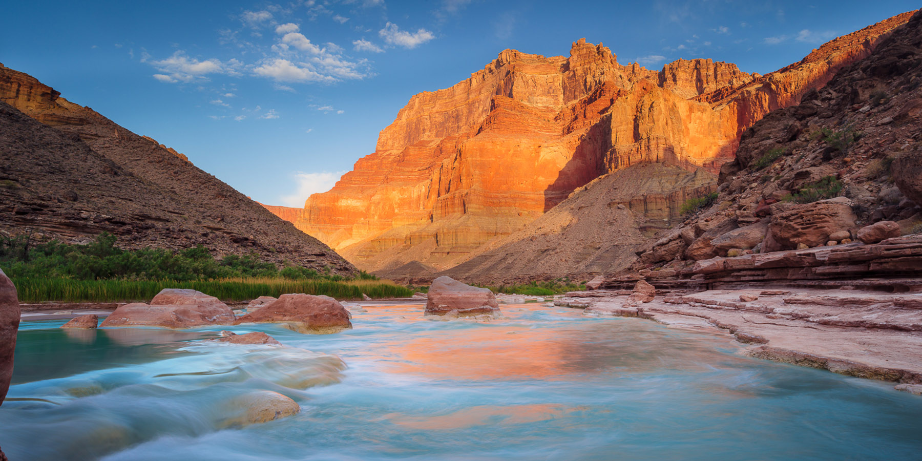 The milky turquoise waters of the Little Colorado River with sunlit cliffs in the background