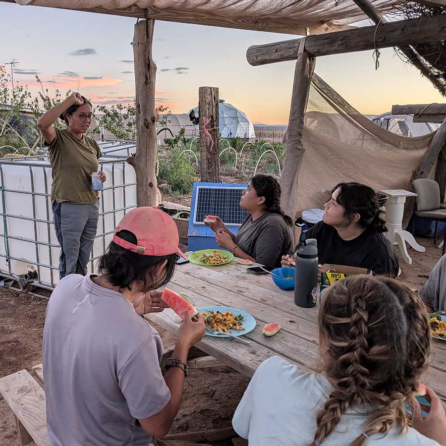 Rising leaders share a meal at a picnic table under a shade structure during LeaderShift 2024