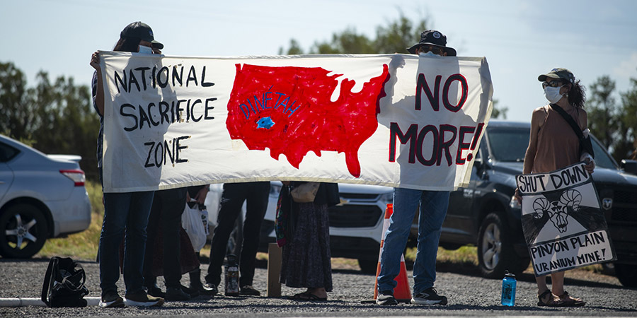 Protestors hold up a banner that says National Sacrifice Zone No More with an image of the United States in red and Dinetah (Navajoland) in blue) during protest against uranium hauling at canyon mine, aka pinyon plain mine