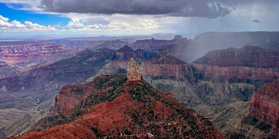 Point Imperial, a whitish chimney of rock on top of bright red rocks, on the North Rim of the Grand Canyon during a monsoon storm, rain and clouds