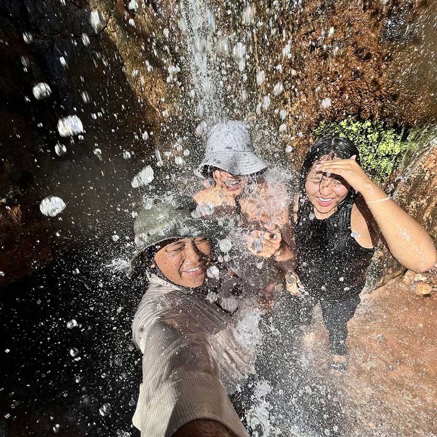 Three young people stand under a waterfall in the Grand Canyon