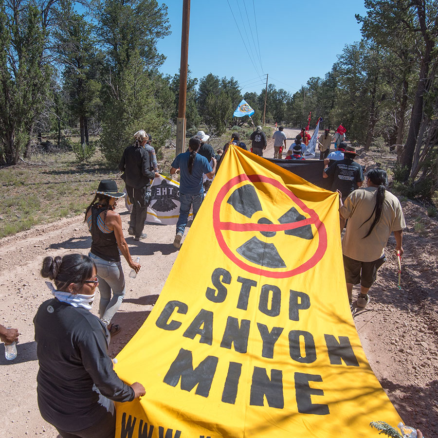 Havasupai activists march along the gravel road that leads to Canyon uranium mine holding a yellow "stop canyon mine" banner.