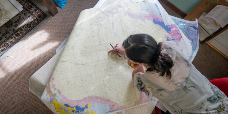 Woman leans over map with a pen in her hand.