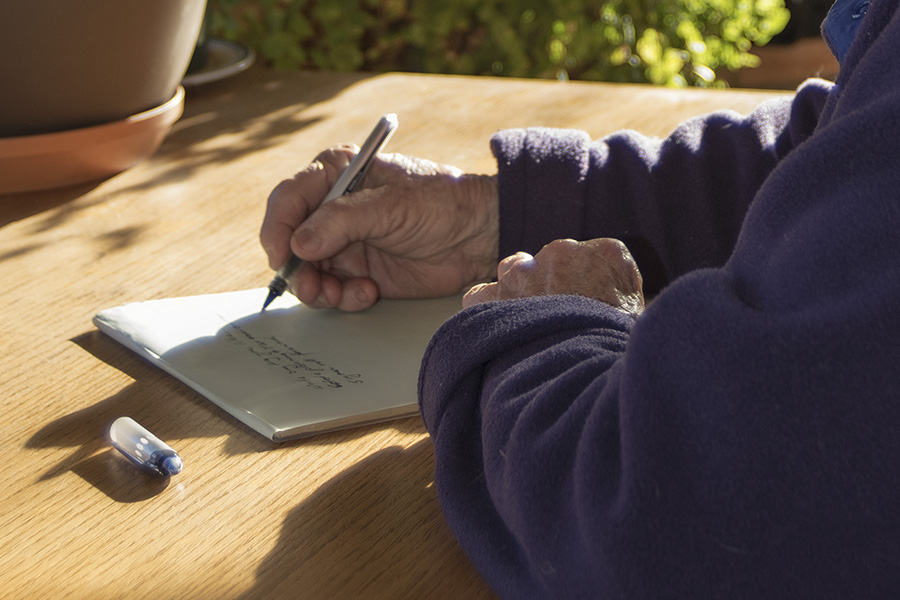 Woman's hands in a purple fleece writing with a pen on a pad.