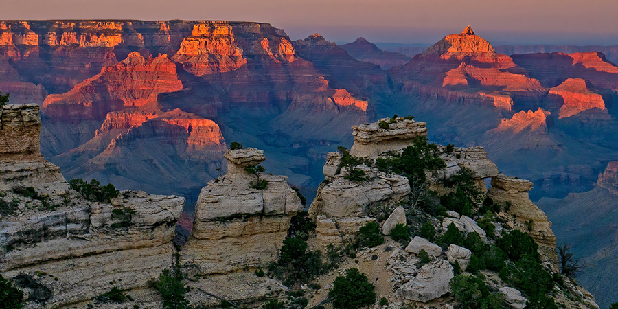 Sunset capping rocks of the Grand Canyon in bright pink with yellow cliffs in the foreground