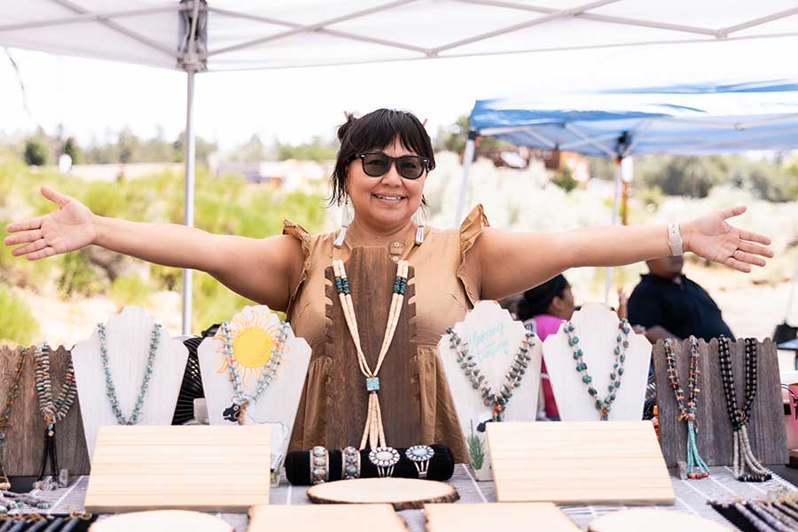 A jewelry vendor stands behind her wares with open arms