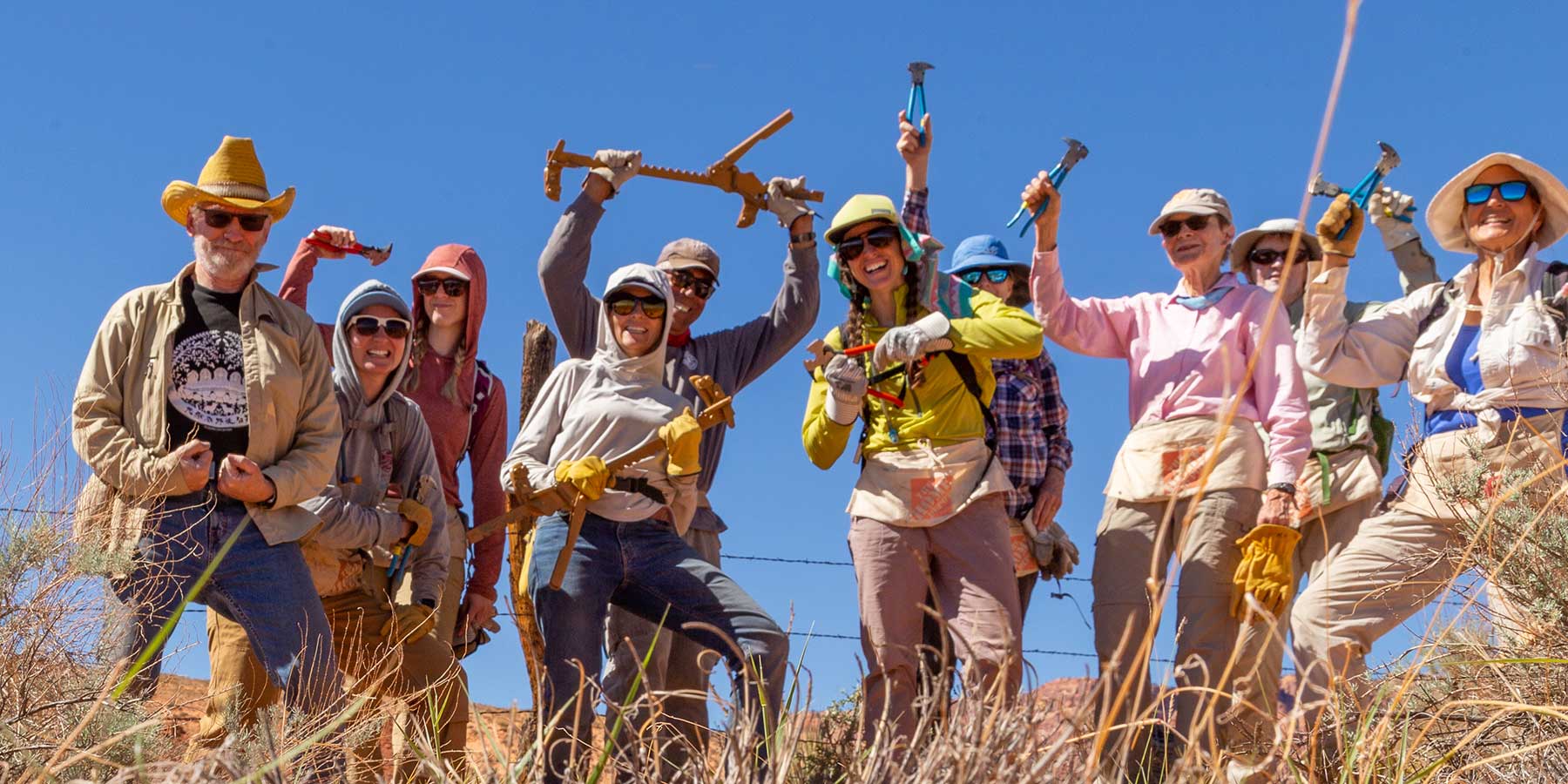 A group of volunteers poses with fence tools and work gloves in a grassland.