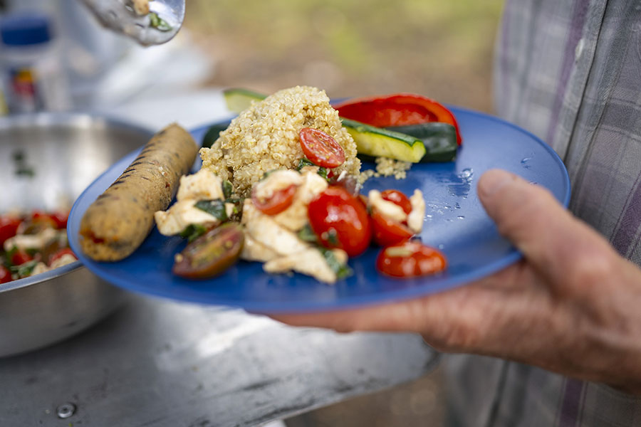 A close up of a dinner plate with couscous, a veggie sausage, and grilled veggies.