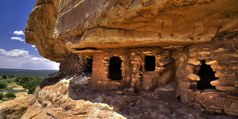 Rock structure built into a rock face under a deep blue sky, showing multiple dark entryways and rugged textures, Bears Ears National Monument.